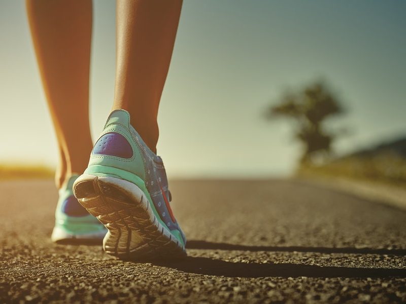 Closeup of female runner shaved feet in running shoes going for a run on the road at sunrise or sunset. Shallow depth of field toned with instagram like filter flare effect.