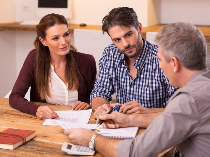 Businessman explaining loan policy to young couple. Happy young couple discussing with a financial agent their new investment. Financial consultant presents bank investments to a young couple.